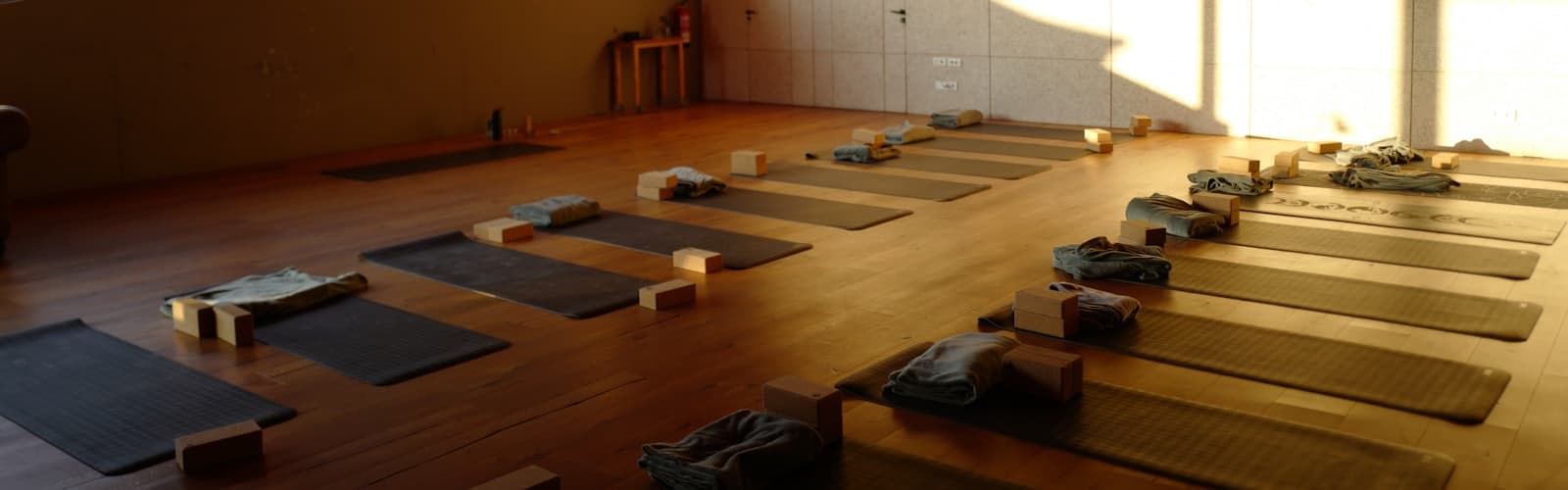 Een zaal met yogamatten en blokken klaargelegd, zonder deelnemers